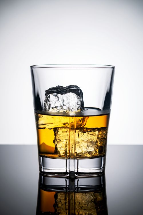 Free Close-up shot of whiskey glass with ice cubes on a reflective surface. Stock Photo