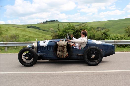A vintage Bugatti roadster speeding through the scenic Tuscan countryside on a sunny day.