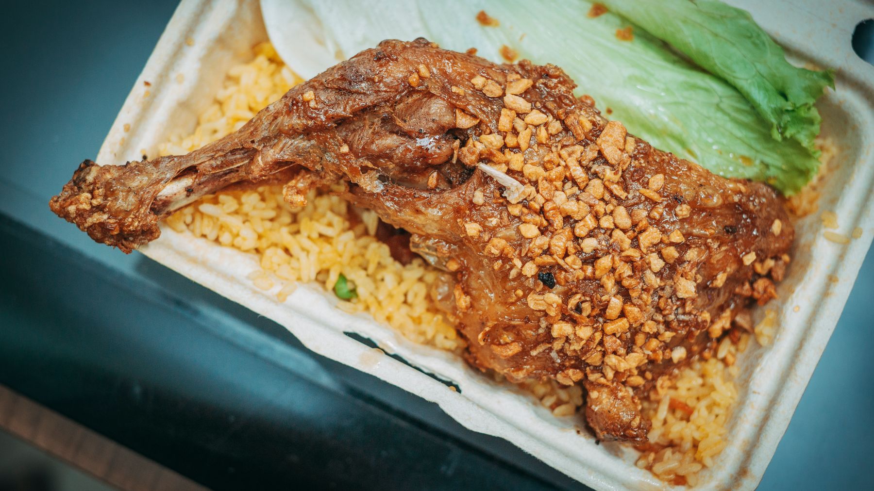 Savor a delicious crispy garlic chicken leg served on a bed of fried rice with fresh lettuce.