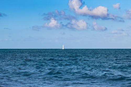 White Sailboat on Sea Under Blue Sky and White Clouds