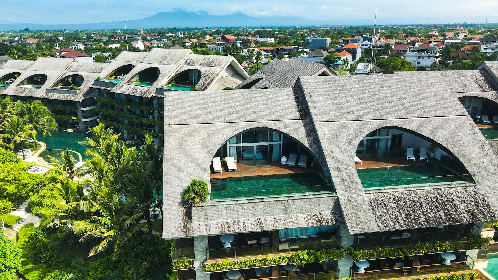 Aerial view of a contemporary resort in Bali, showcasing unique design with lush green landscapes and a pool.