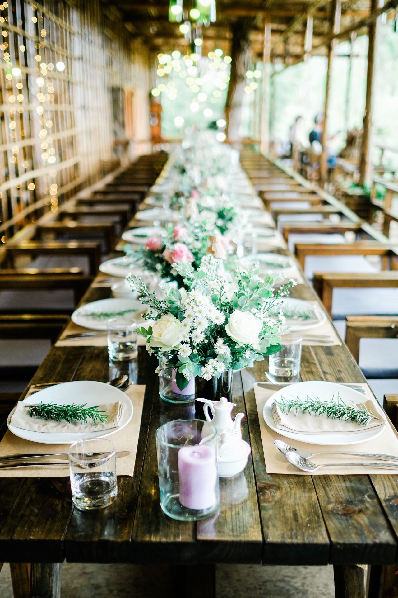 Long dark plank wood table set with plates, flowers, and candles