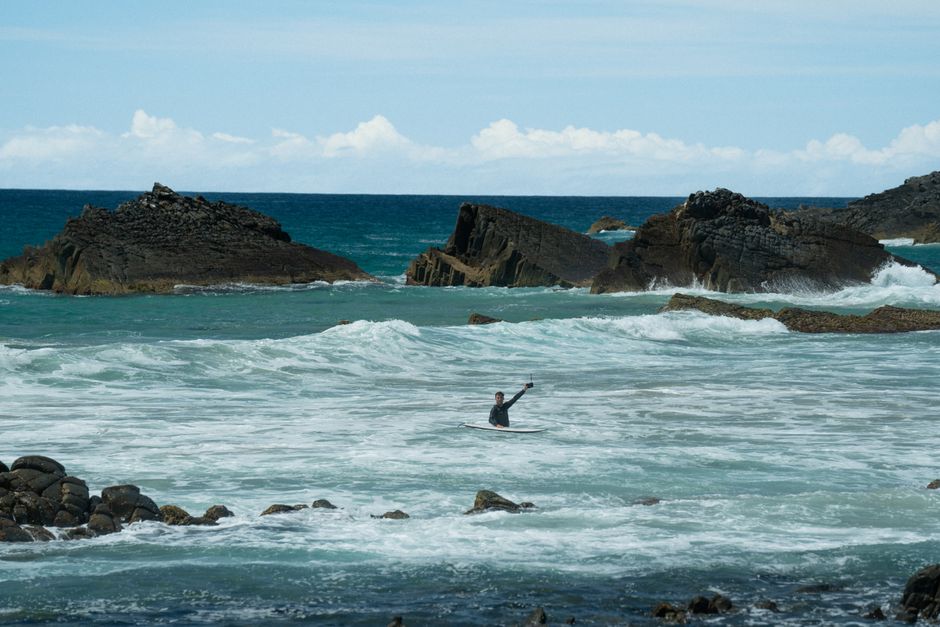 A surfer rides the ocean waves surrounded by rocky formations on a sunny day.