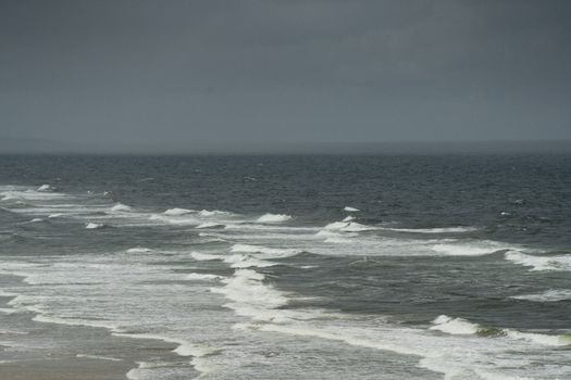 A serene view of ocean waves crashing onto the shore under a moody overcast sky.