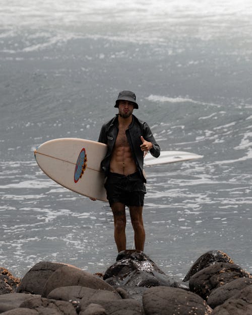 A Man Holding a Surfboard Standing on the Rocks