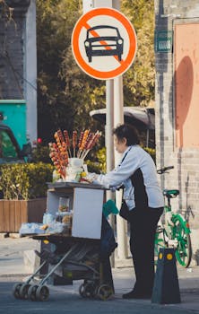 A street vendor in Beijing selling candied fruit from a cart in an outdoor market setting.