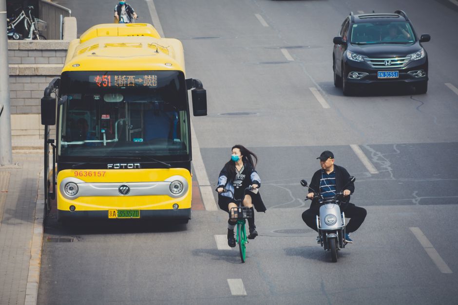 A busy Beijing street featuring cyclists, scooter, bus, and a car.