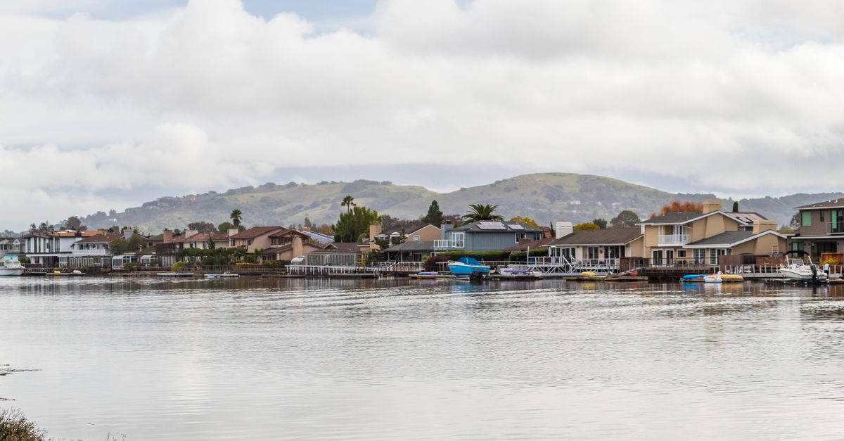 A scenic view of waterfront homes against a mountain backdrop with boats docked on a calm water body.
