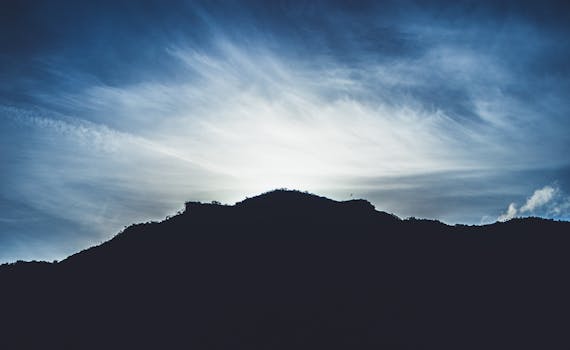 A stunning silhouette of a mountain with a backlit sky at sunrise creating a dramatic scene.