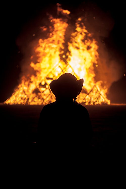 Silhouette of Person Wearing Hat Near a Fire