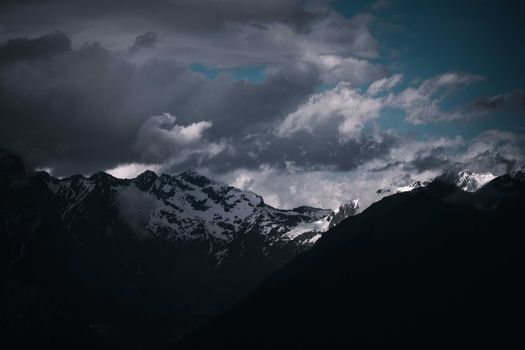 Breathtaking view of snow-capped mountains under a moody sky with dramatic clouds, perfect for nature enthusiasts.