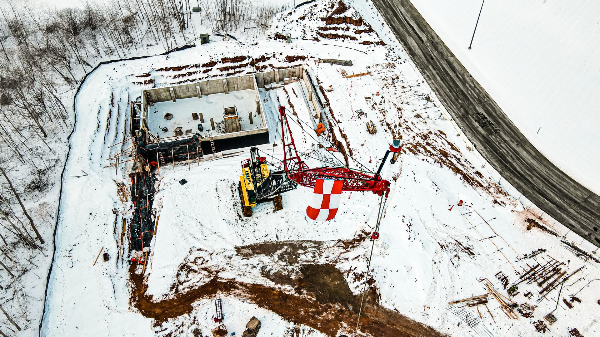 Aerial view of a snowy construction site in Green Bay, showcasing cranes and heavy machinery.