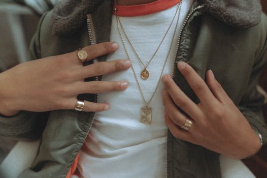 Close-up of elegant hands showcasing gold rings and necklaces, highlighting fashion style.