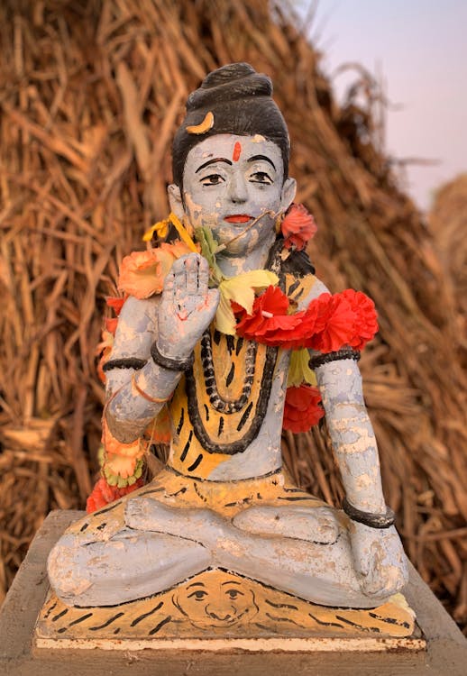 A Buddha Statue with Lei Near a Stack of Hay
