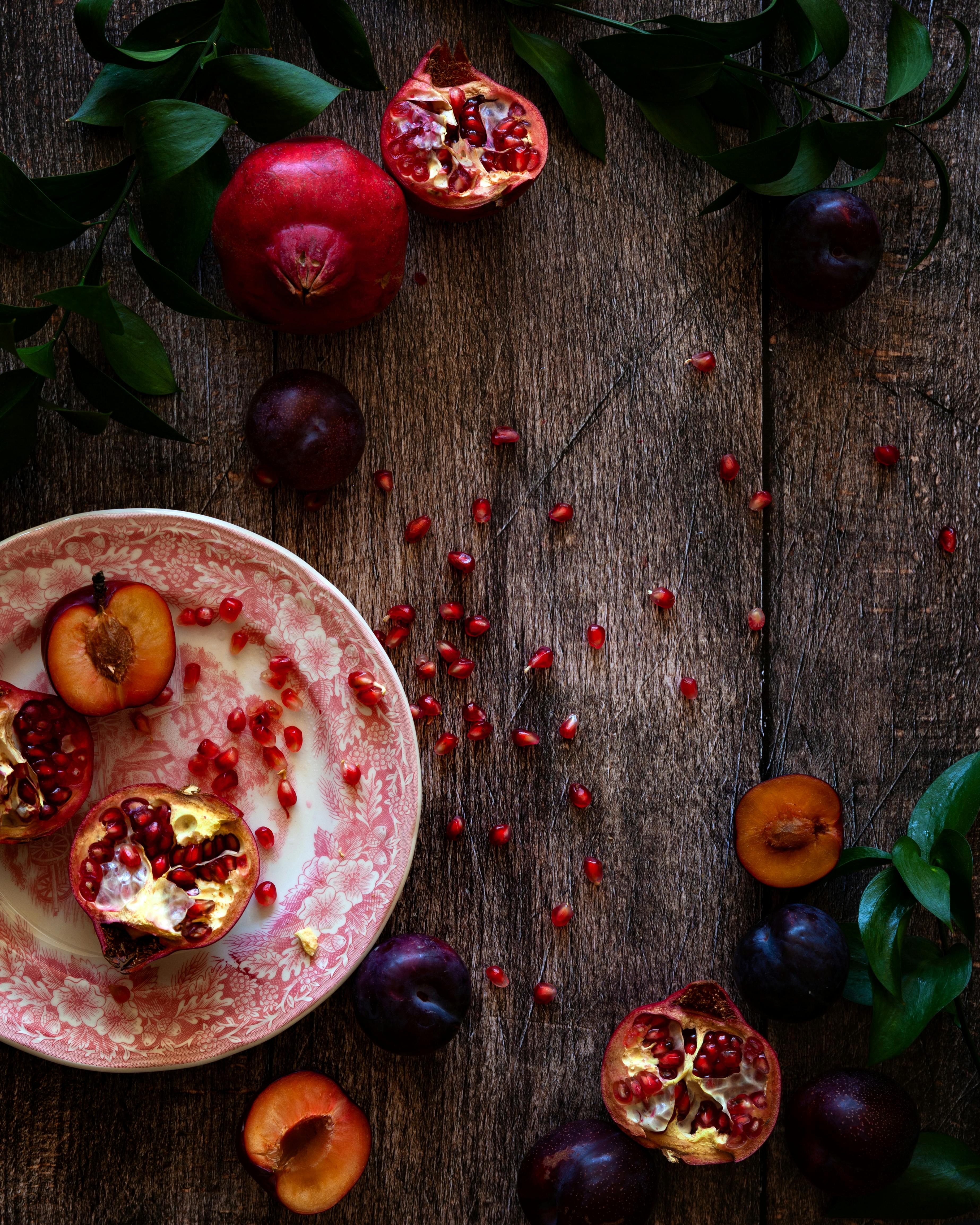 A vibrant composition of pomegranates and plums on a rustic wooden table with greenery.