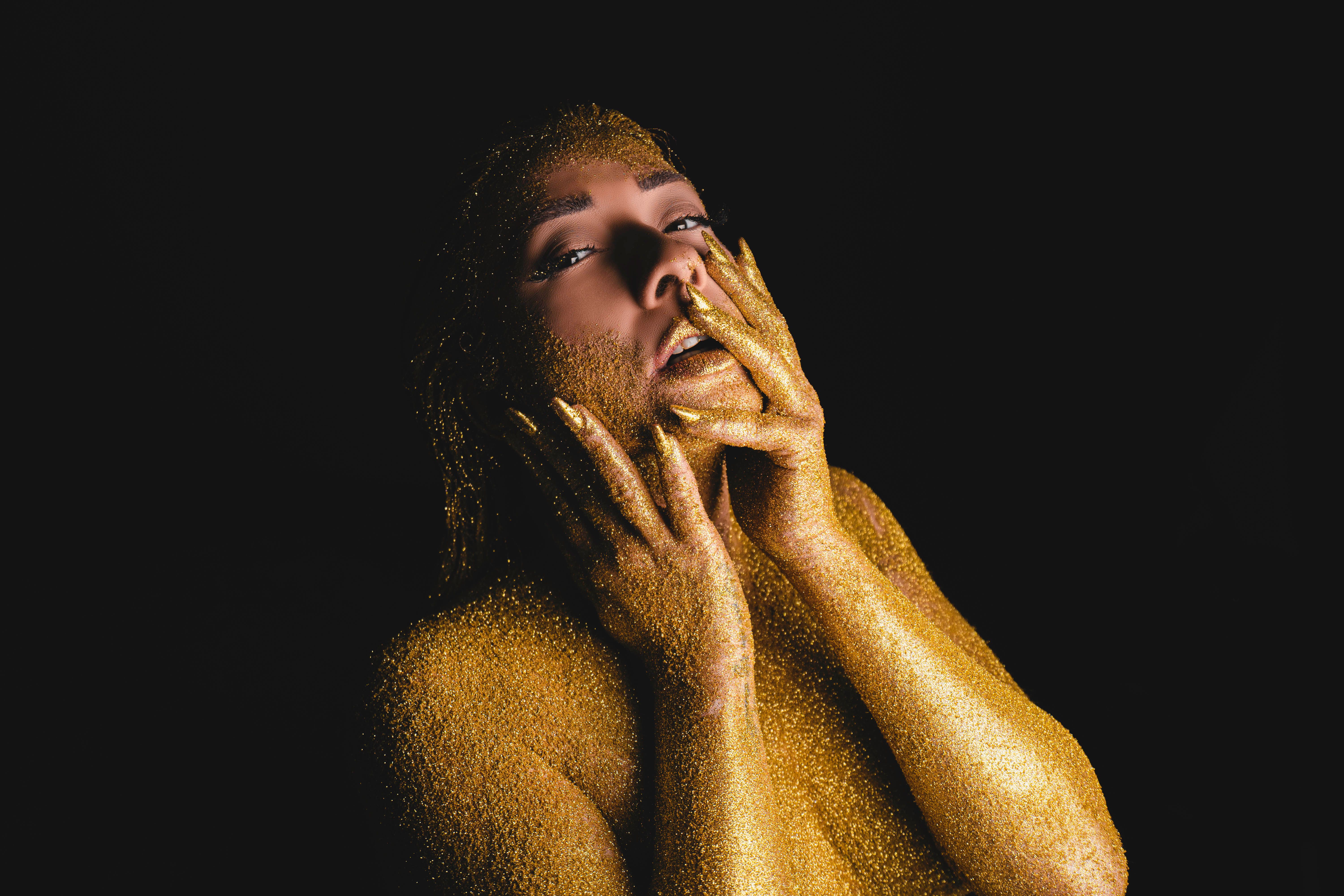 A dramatic portrait of a woman covered in golden glitter on a black background.