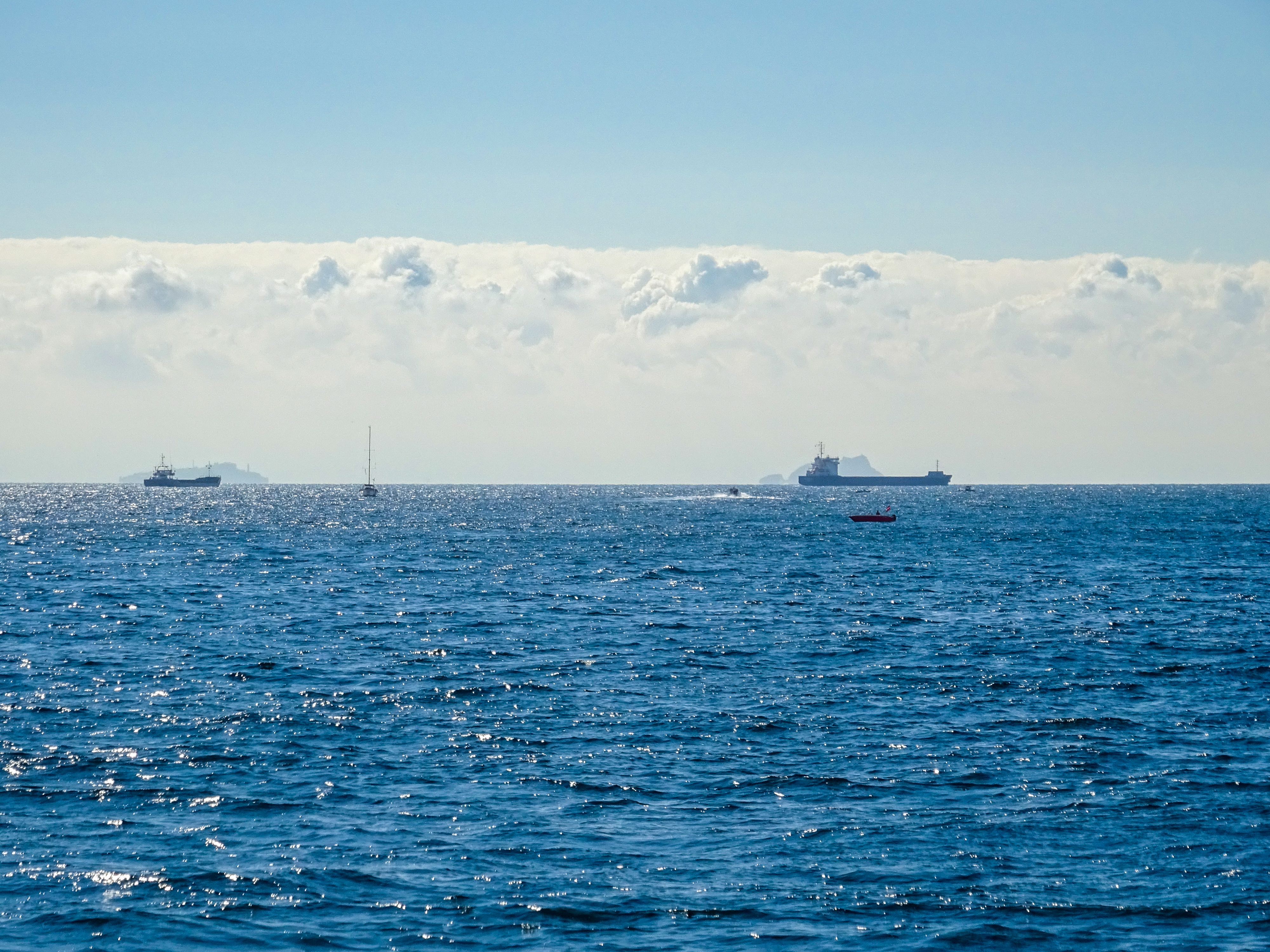 A calm ocean scene featuring ships on the horizon under a bright blue sky with scattered clouds.