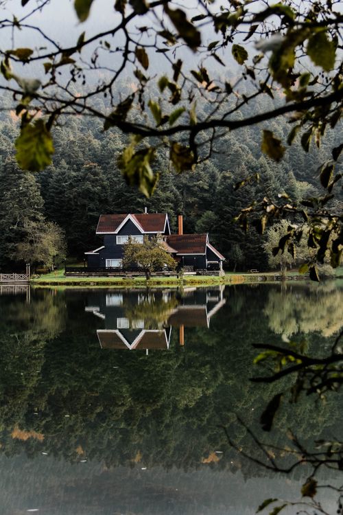 Free A serene house reflected in a tranquil lake surrounded by dense forest, creating a peaceful scene. Stock Photo