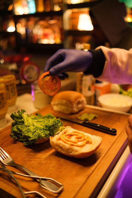 Free A chef adds fresh ingredients to a gourmet burger under warm lighting in a cozy restaurant setting. Stock Photo