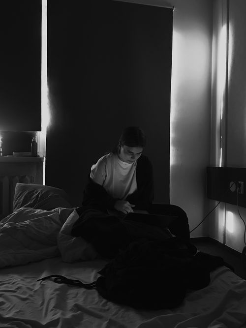 Free Woman sitting in a dark bedroom using a laptop, creating a moody, focused atmosphere. Stock Photo