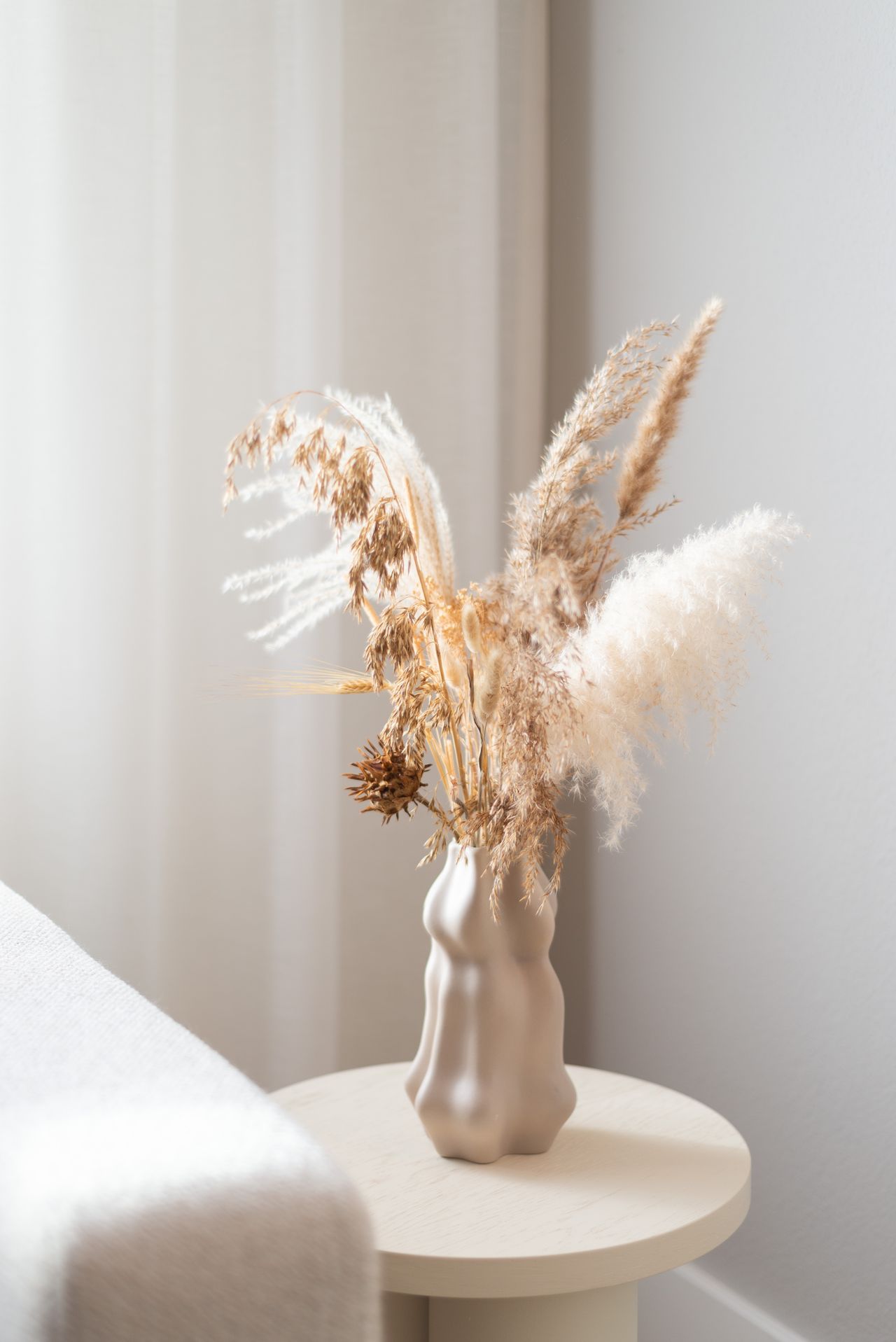 Dried pampas grass bouquet in a sculptural white ceramic vase on a round side table
