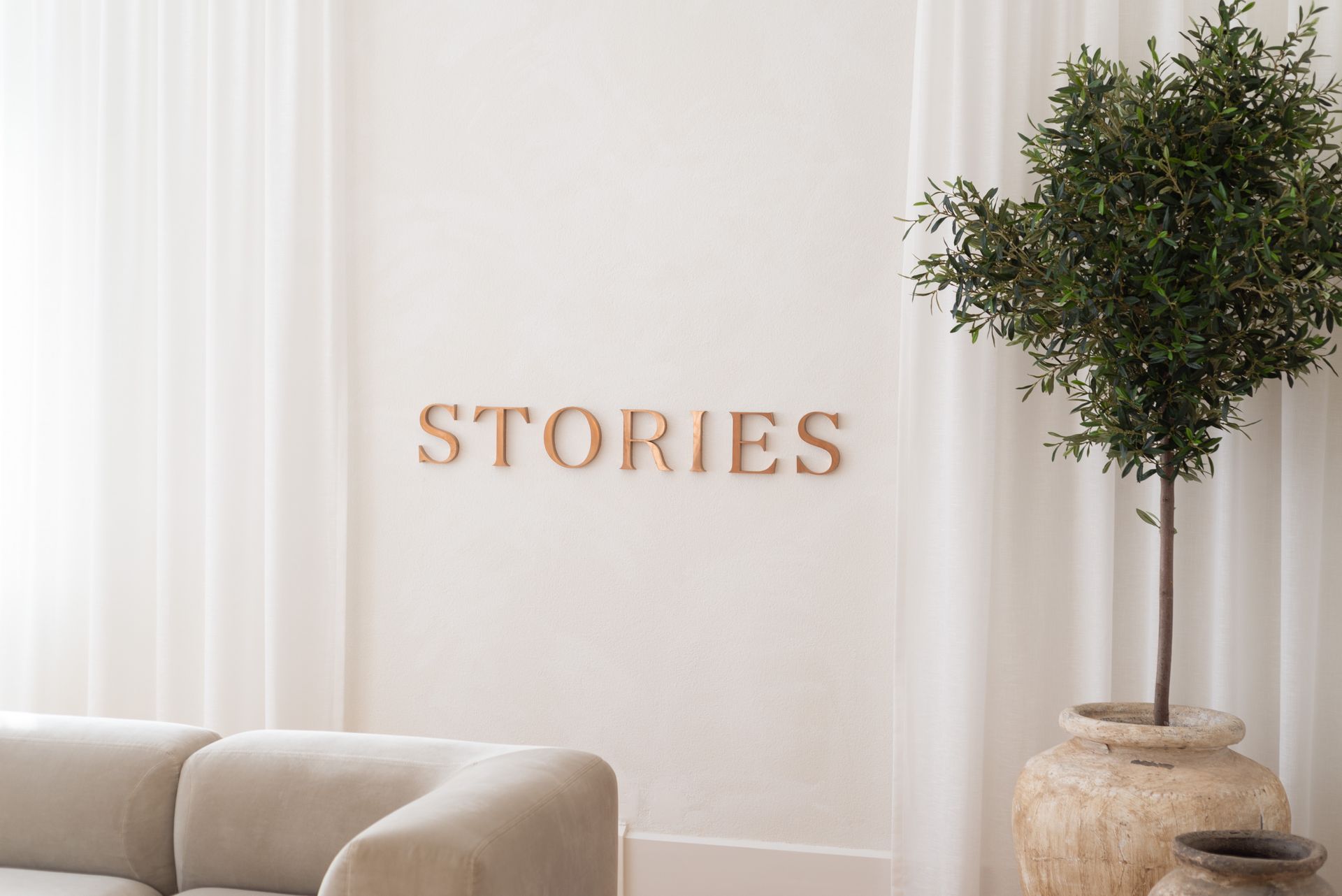 A cozy minimalist living room featuring a potted tree and 'Stories' wall decor.