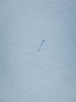 A lone snow kite glides over a vast, snow-covered terrain, casting a long shadow.