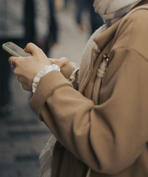 Free A person using a smartphone outdoors in a city setting, wearing a stylish coat. Stock Photo