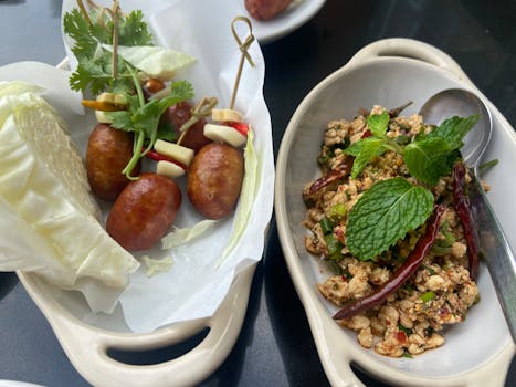 Explore authentic Thai cuisine with spiced sausages and herb-seasoned dishes, garnished for a delightful meal.