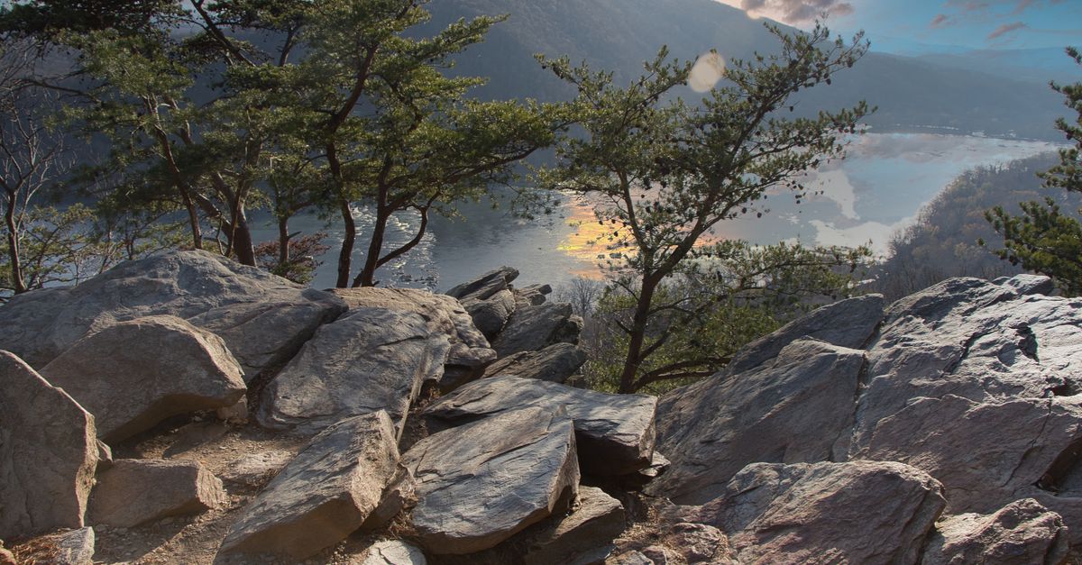 Serene landscape of rocky cliffs and pine trees overlooking a calm river under a vibrant sky.