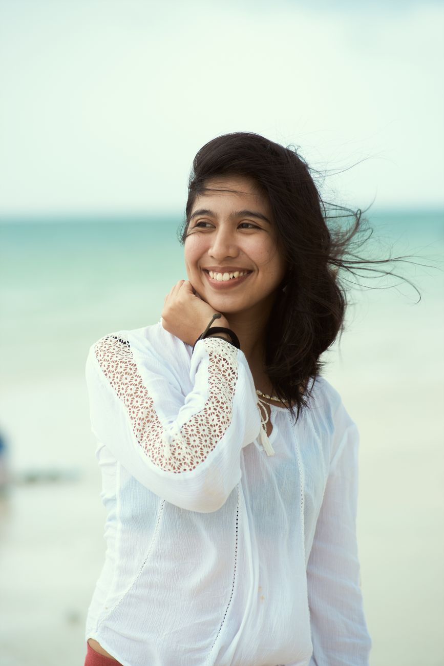 Smiling woman on a windy day at the beach, showcasing fashion and happiness.