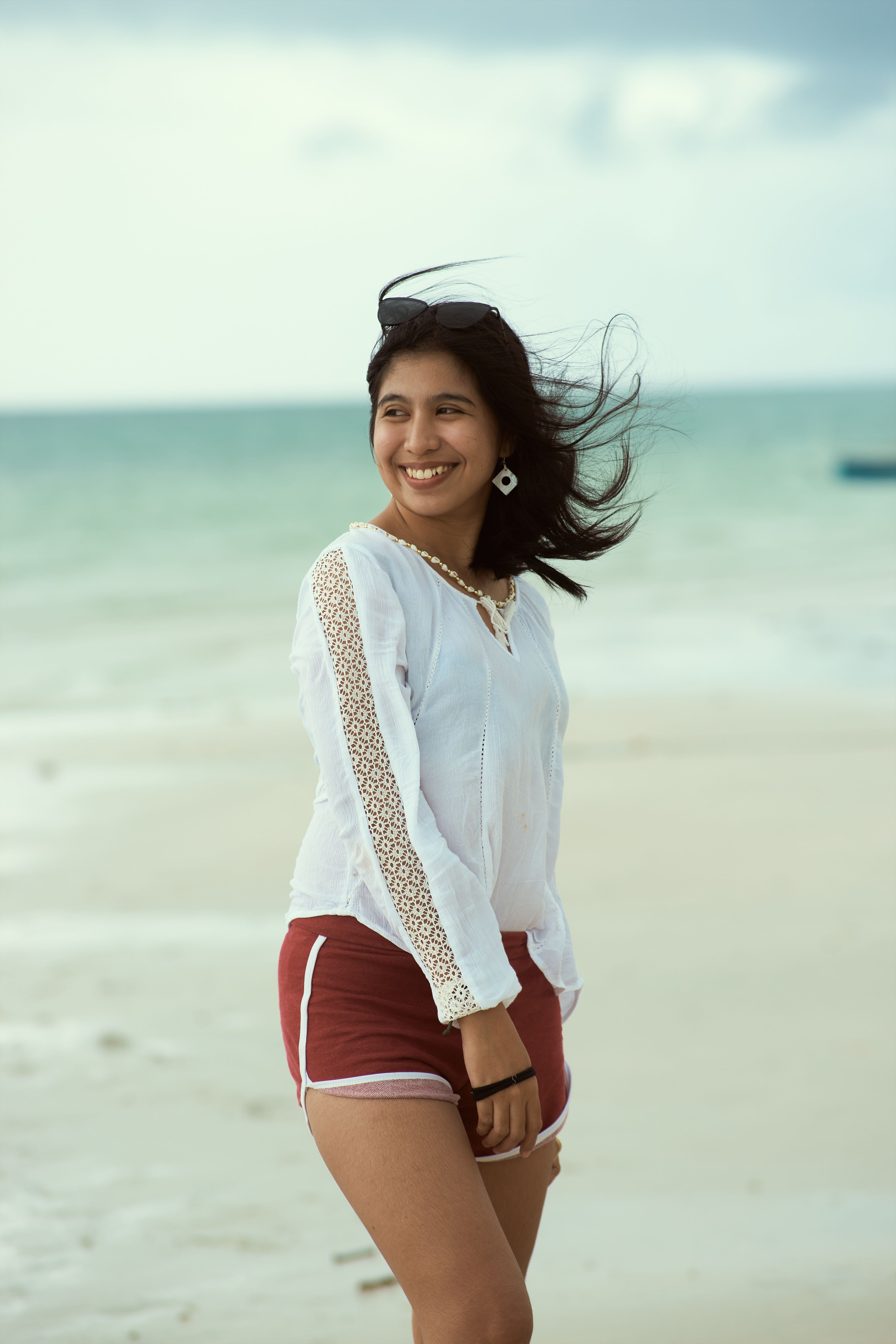 Happy woman with flowing hair and white blouse enjoying a breezy day on the beach.