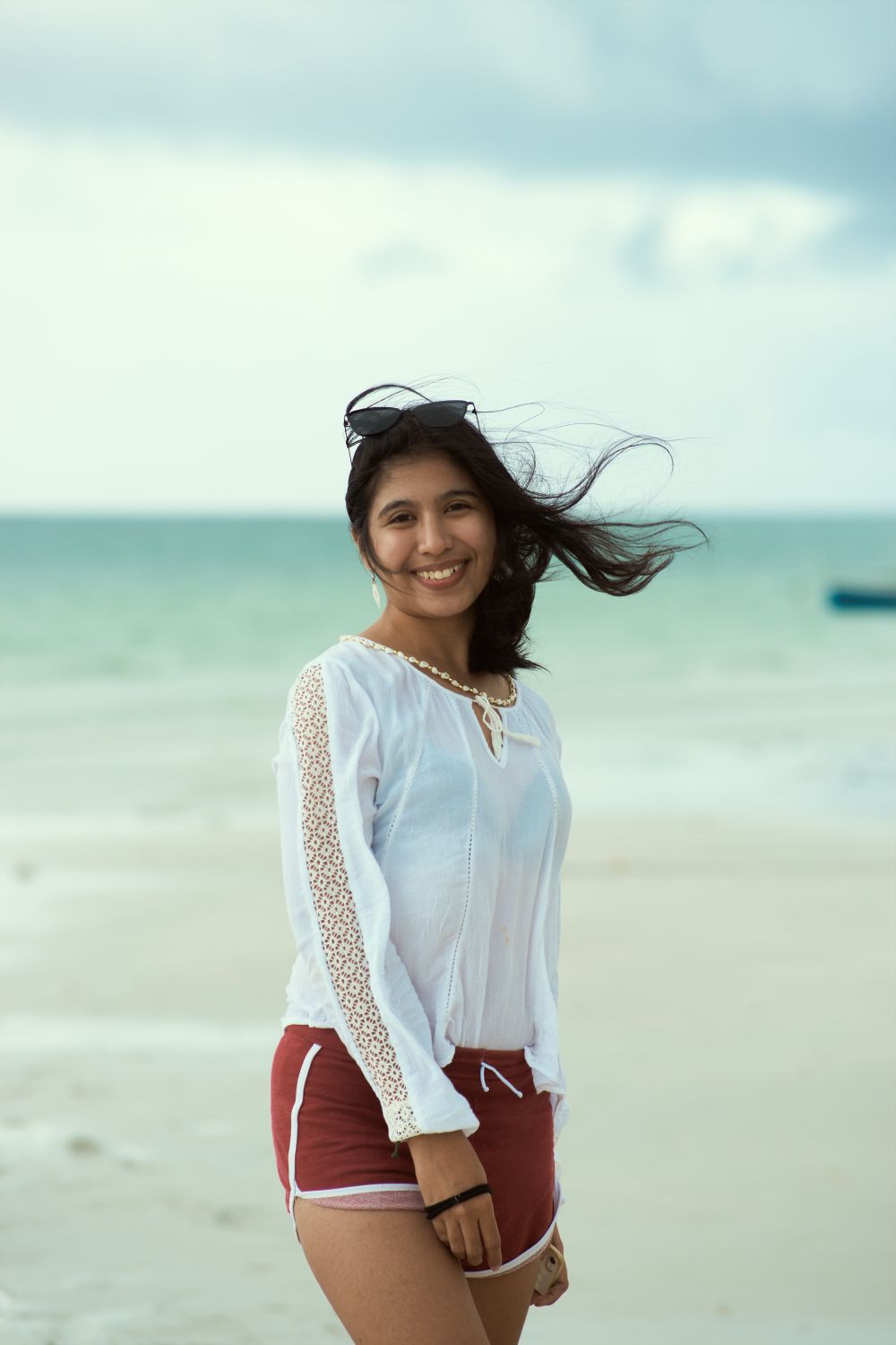 Woman in casual long sleeve shirt posing happily on a windy beach with ocean view