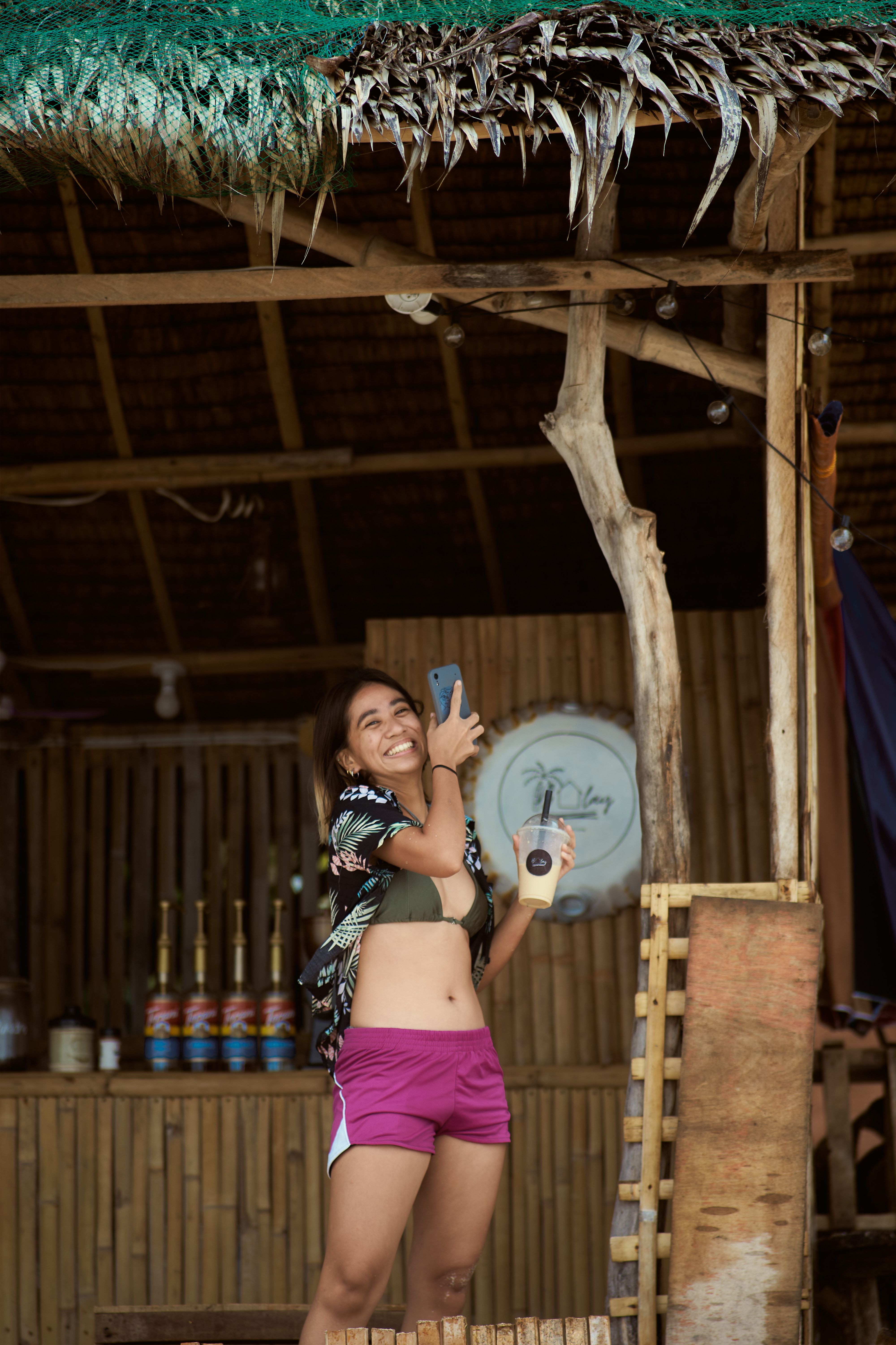 Happy woman taking a selfie at a rustic beach bar, capturing summer vibes and leisure moments.