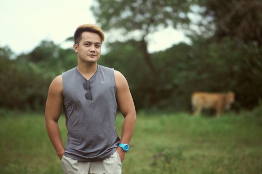Man in gray tank top standing in a green field with relaxed pose.