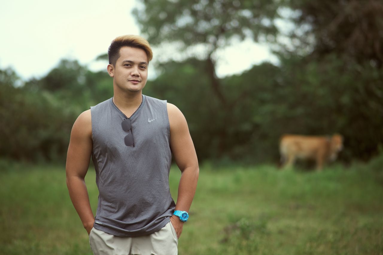 man in gray tank top standing in a green field with relaxed pose