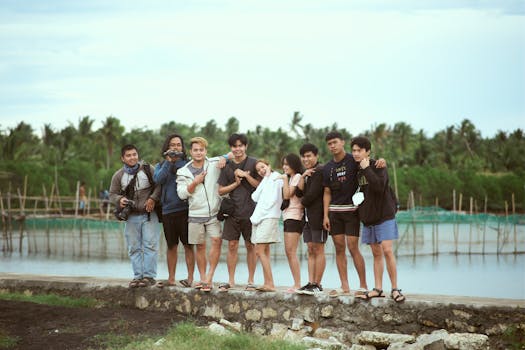 A joyous group of seven friends posing near a fish pond with greenery and wooden structures.