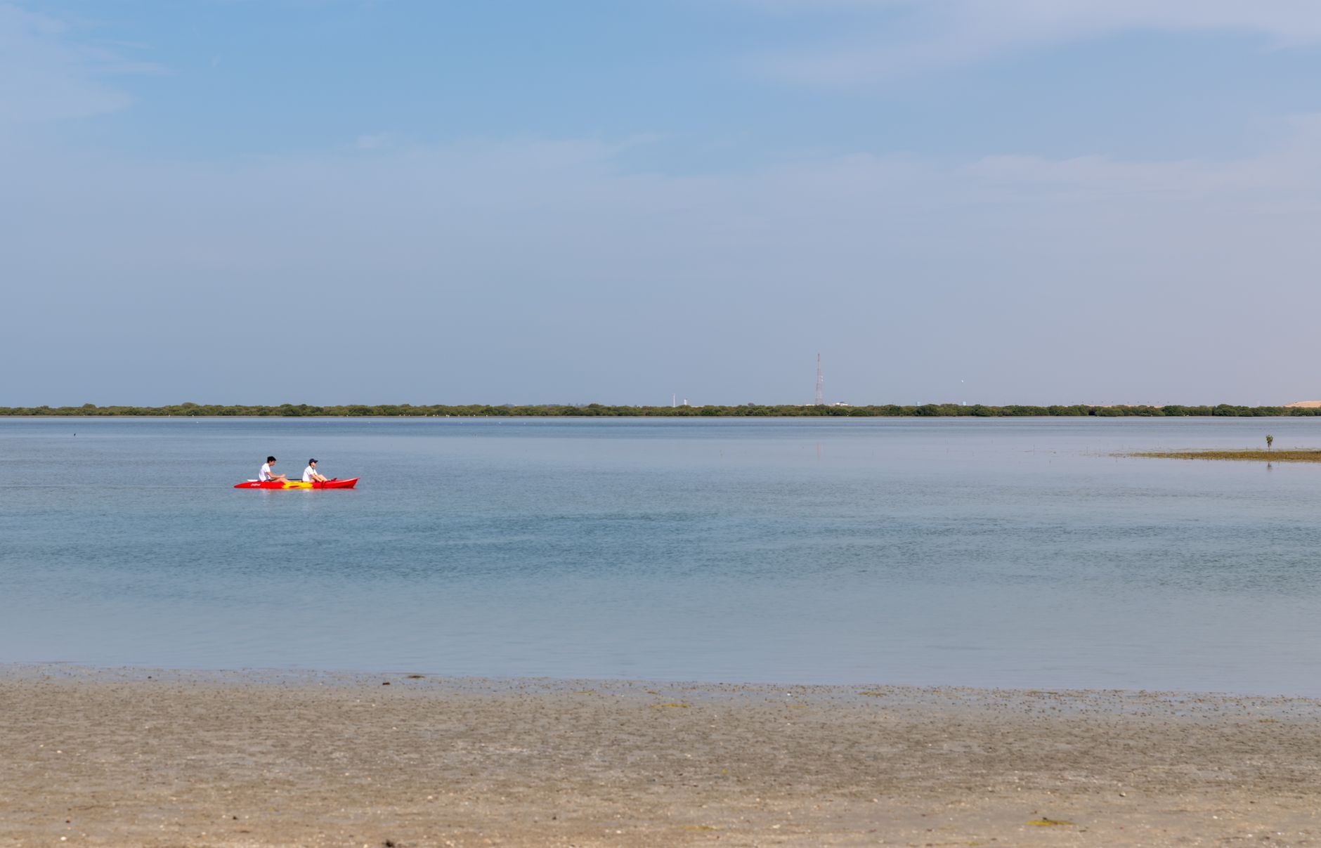 Two kayakers paddle on a calm lake in Umm Al Quwain, UAE, under a clear sky.