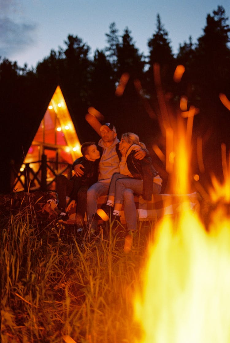 A Family Sitting Near The Grass With Bonfire