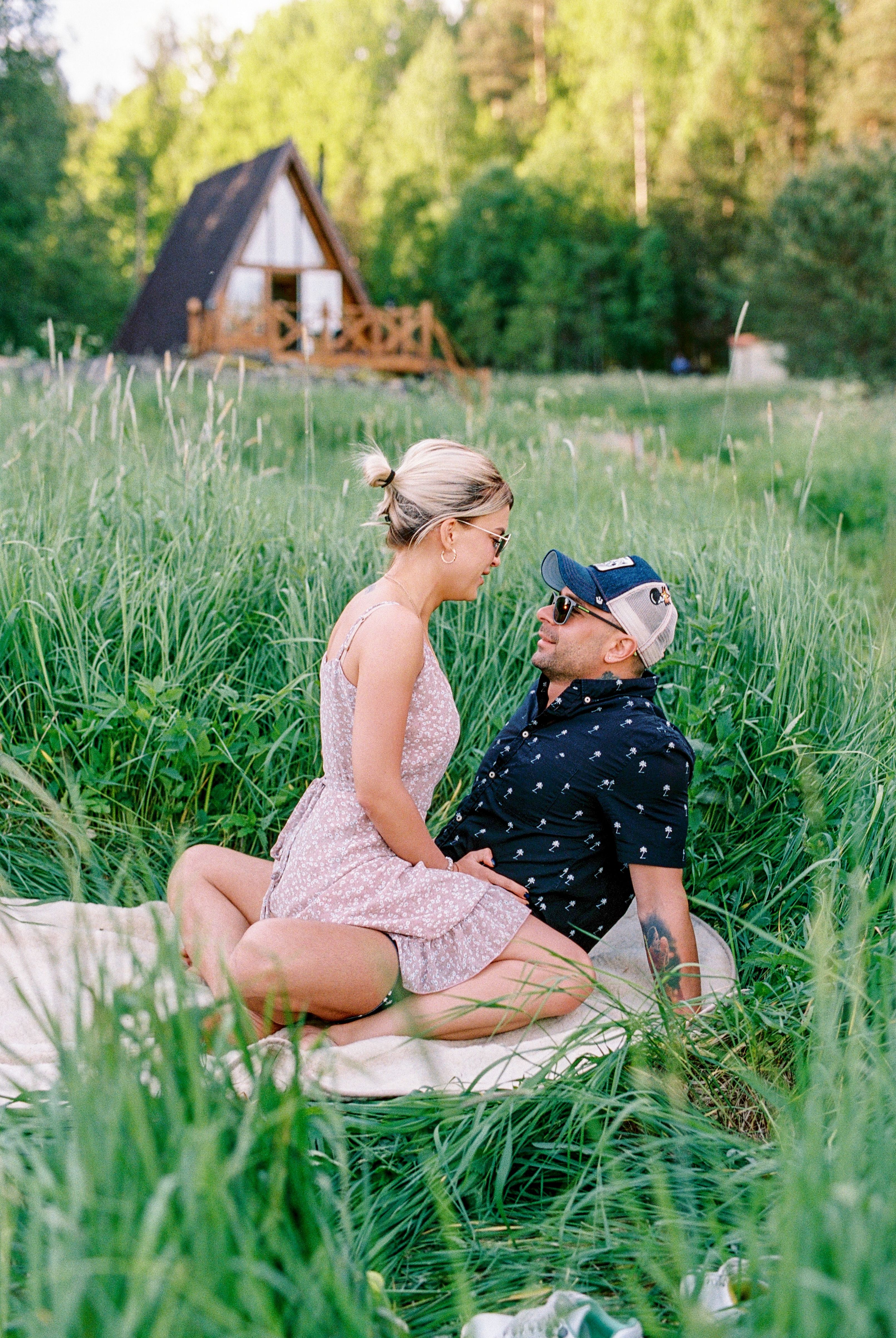 A couple enjoying a romantic moment in a sunny meadow near a wooden cabin.