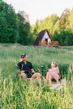 A couple enjoying a sunny day in a meadow next to an A-frame cabin, illustrating leisure and nature.