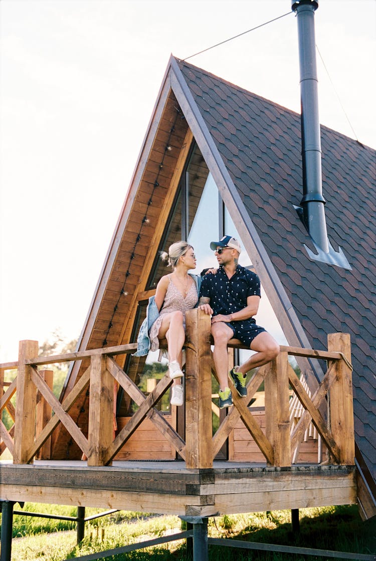 Man And Woman Sitting On A Wooden Railing