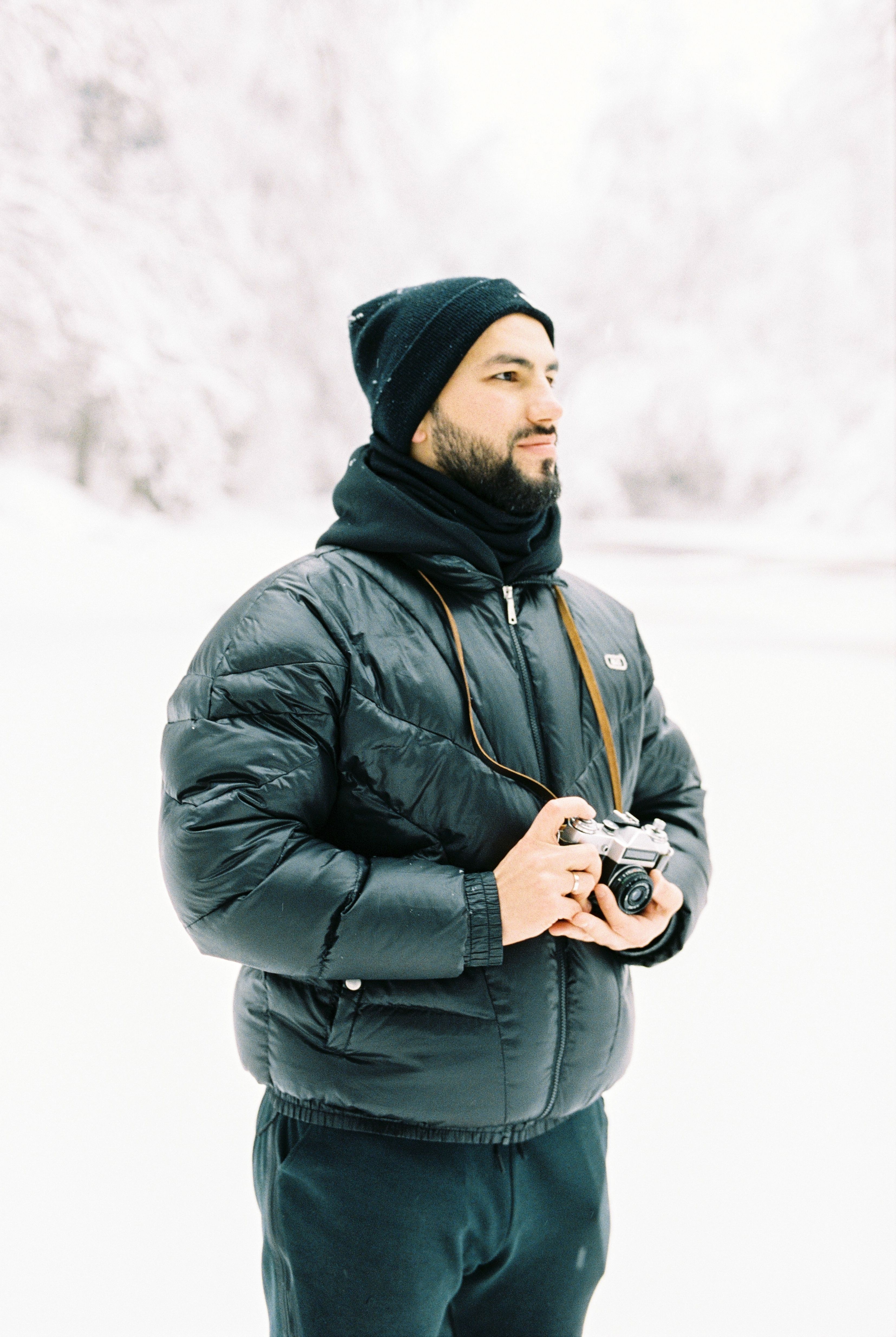 Man standing in snowy forest holding a vintage camera, dressed warmly.