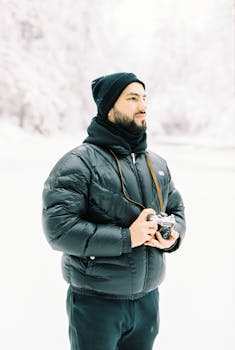 Man standing in snowy forest holding a vintage camera, dressed warmly.
