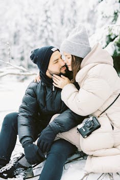 A loving couple in warm clothing shares a tender moment in a snowy forest setting.