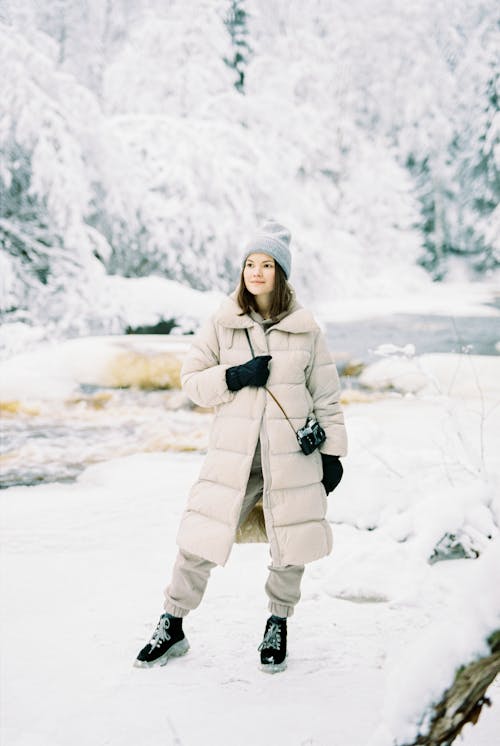 A Woman in Puffer Jacket and Knitted Cap Standing on a Snow Covered Ground