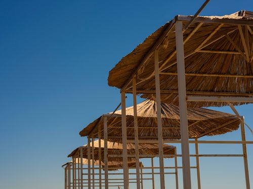 Free Serene view of tropical beach huts with thatched roofs against a vibrant blue sky. Stock Photo