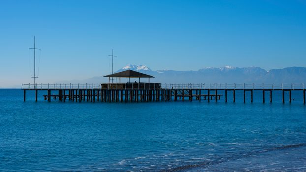 A picturesque ocean view with a pier stretching into calm waters and a mountain backdrop.