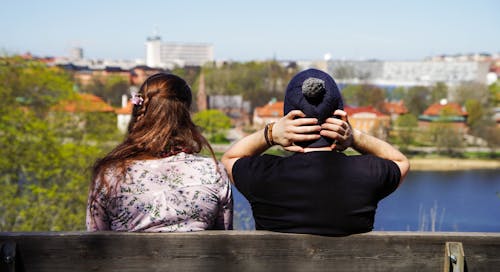 Two People Sitting on Bench Facing on Body of Water