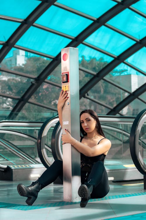 A Woman in Black Tank Top and Black Pants Sitting Near an Escalator